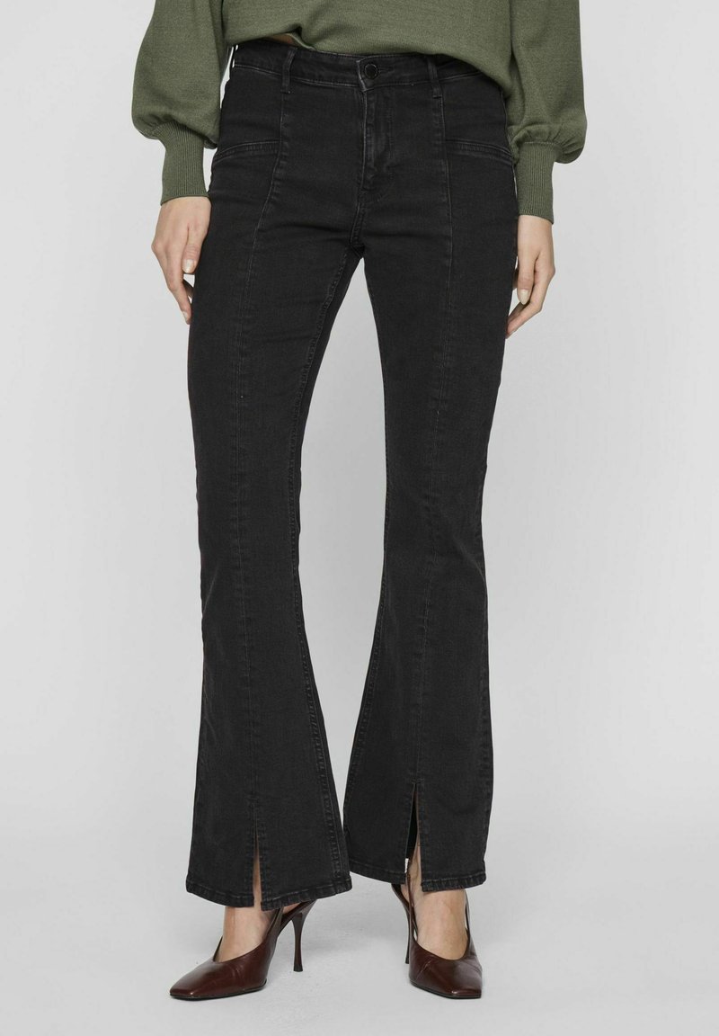 Melnas izsistās džinsus ar augstu jostasvietu, izgriezumiem pie potītēm un mīkstas tekstūras džinsu audumu. Saskaņoti ar vērpjo bordo krāsas augstpapēžu kurpēm.