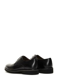 Zapatos de cuero negro con una textura suave, punta redondeada y tacón bajo. Cuentan con un clásico diseño de cordones y sutiles acentos de costura.