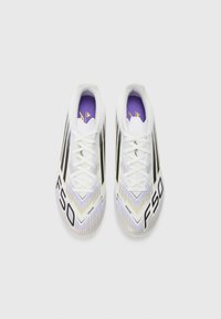 Des crampons de soccer blancs avec des accents noirs et violets, présentant un design élégant, une surface texturée et un marquage "F50" bien visible sur les côtés.