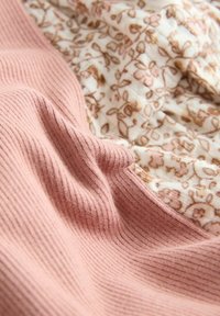 Tejido de punto en color rosa suave con canalé vertical, superpuesto sobre una tela crema adornada con un delicado patrón floral en rosa y marrón.