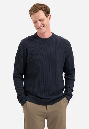 Navy ribbels gebreid sweater met een ronde hals en lange mouwen, gecombineerd met lichtbeige broeken. Het ontwerp heeft een textuurstof door het hele kledingstuk.
