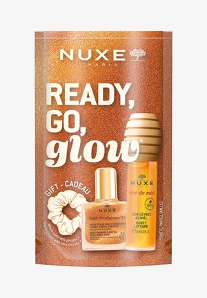 NUXE cadeaupakket met glinsterende bronzen verpakking, een flesje gouden olie, een tube honing lipverzorging en een haarelastiek.