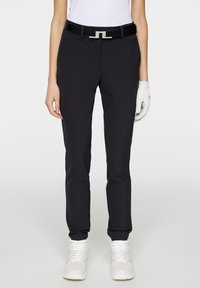 Black golf pants with a slim fit, made from a smooth material. Features a black belt with silver hardware. Paired with white sneakers.