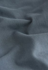 Sötétszürke szövet, sima textúrával és finom fényű felszínnel, finom bordázott mintázattal, amely puha redőket és hullámokat formasít.