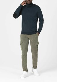 Navyblauer Rollkragenpullover mit strukturierten Schulterakzenten und Ellbogenpatches, kombiniert mit olivgrünen Cargo-Hosen mit Seitentaschen und Bündchen.