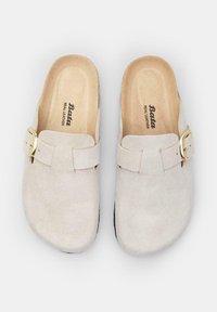 Beige suede clogs with a gold buckle, featuring a soft textured upper and a black rubber sole, labeled "Bata Real Leather."