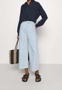 Světle modré široké džíny, námořnická button-up košile, černá a béžová tkaná taška a černé sandály se zlatými akcentmi.