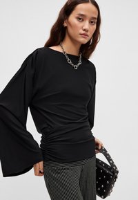 Must pikkade varrukatega tume ülemine osa, mis on valmistatud venivast kangast, kujunduses paadikaelus ning vöökoha lähedal kogumismustriga. Sobitatud triibuliste pükste ja naelutatud käekotiga.