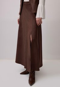 Rjava, semišasta maxi krilo z bočnim razporkom, združena z oprijetimi rjavimi gležnjarji. Ima gladko teksturo in krojen pas.