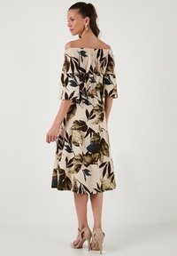 Floral off-the-shoulder dress in cream with brown and blue leaf patterns, featuring a fitted bodice and tiered skirt. Worn with beige heels.
