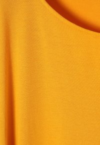 Helles, gelbes Material mit einer weichen Textur; verfügt über einen weiten, abgerundeten Ausschnitt und eine glatte Oberfläche ohne Muster oder Verzierungen.