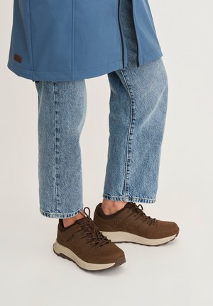 Bruine veterschoenen voor casual gebruik, gedragen met lichtblauwe spijkerbroek en een blauwe jas, getoond van halverwege de kuit naar beneden tegen een neutrale achtergrond.