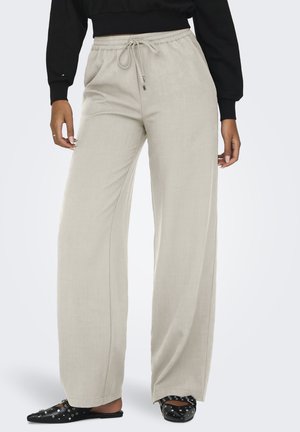 Pantaloni beige a gamba larga con vita elasticizzata e cordoncino, indossati con ballerine nere a punta con borchie e un top nero a maniche lunghe.