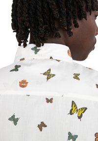 Camisa de algodón blanca con estampado de mariposas y osos, con cuello y cierre de botones. Los patrones incluyen mariposas de varios colores y tamaños.