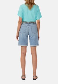 Lichtblauwe denim shorts met opgerolde zomen, met achterzakken. Gecombineerd met een turquoise T-shirt met korte mouwen en een zwart met patroon riem.