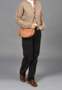 Cárdigan de punto marrón, pantalones de sarga negros y zapatos de cuero marrones. Un pequeño bolso de cuero tostado con un acabado texturizado cuelga del hombro.