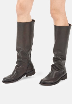 Hohe dunkelbraune Lederstiefel, getragen an bloßen Beinen, mit seitlichem Reißverschluss und niederen Absätzen.