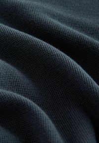 Katoenen stof in diep marineblauw, met een textuurweefsel en een zichtbaar kruispatroon, zachtjes vallend in elegante plooien.