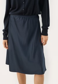Marinblå satin kjol med elastisk midjeband, slät yta och knälång design, matchad med en mörk knapp-up kofta.