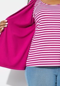 Cardigan fucsia sobre una camiseta a rayas blanca y rosa, con una forma relajada. La persona lleva unos vaqueros de color azul claro.