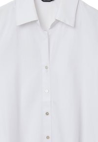 Chemise blanche à manches longues en tissu lisse, avec un col pointu et six boutons sur le devant. Sans motifs ni embellissements.