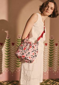 Roze emmer tas met bloemmotief en rode accenten, voorzien van een trekkoordsluiting; gemaakt van lichtgewicht stof en heeft een ronde vorm.