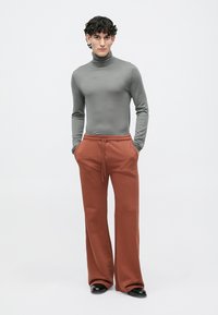 Šedý dlouhý rukáv s rolákem v kombinaci s volnými, měděně zbarvenými tepláky. Tepláky mají boční kapsy a elastický pas. Černé boty.