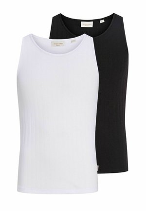 Junger Mann mit runden Sonnenbrillen, weißem Tanktop, schwarzem Gürtel, lockeren schwarzen Jeans und schwarzen Schuhen, stehend vor einem schlichten hellen Hintergrund.