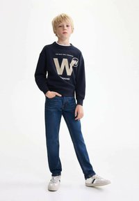 Felpa navy con testo bianco e oro, inclusi 'W' e 'WEEKEND', abbinata a jeans blu e sneakers grigie con dettagli a righe.