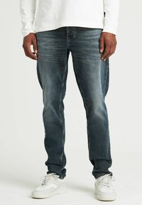 Jeans din denim albastru cu o talie subțire, design estompat și ușoare umbre. Asortați cu adidași albi într-un stil curat.