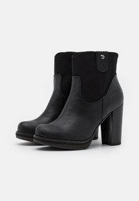 Par de botas negras de tobillo con tacones de bloque, panel trasero texturizado y tirador con botón sobre fondo blanco liso.