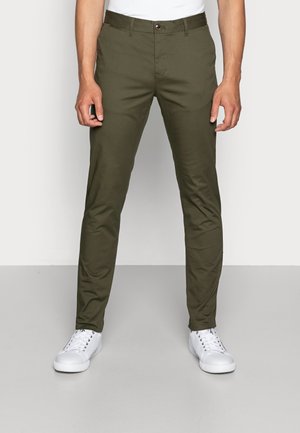 Khaki groene broek gemaakt van een gladde, lichte stof, met een knoopsluiting en zijzakken, gecombineerd met witte sneakers.