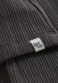 Tissu côtelé gris avec une surface texturée, arborant une étiquette portant la mention "Nips & Co. Ltd" cousue sur le bord.