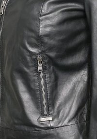 Černá kožená bunda s texturovaným povrchem, s kapsou na zip a kovovou štítkovou značkou blízko zipu. Hladký povrch.