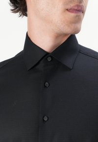 Svart skjorta med knappar, gjord av texturerat tyg, med klassisk krage, fem knappar och utan synliga mönster eller dekorationer.