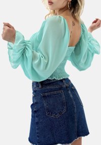 En mintgrøn, gennemsigtig bluse med pufærmer og smockdetalje ved taljen. Kombineret med et højtsiddende mørkt denim-mininederdel med frynset kant.