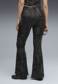 Black flared leggings with a textured, dotted pattern, made from stretchy material. Paired with black shoes and sunglasses in hand.