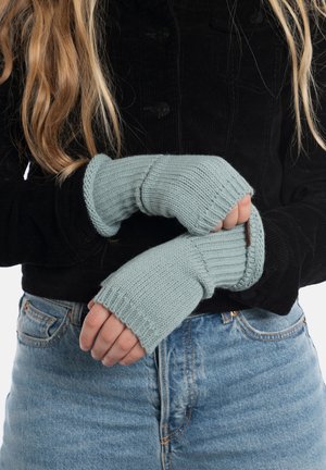 Helles blau gestrickte fingerlose Handschuhe mit gerippten Bündchen und strukturiertem Finish. Getragen mit einer schwarzen Cordjacke und Jeans.