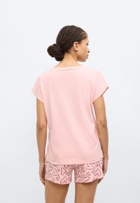 Ροζ κοντομάνικη μπλούζα από μαλακό βαμβάκι, συνδυασμένη με ροζ σορτς με σχέδιο καρδιάς σε κόκκινο. Ομαλή υφή, άνετη εφαρμογή.