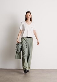 Biela tričko s výstrihom do V a malým logom, v páre s voľnými svetlozelenými nohavicami a zodpovedajúcim oversized sakom. Čierne topánky dotvárajú celkový vzhľad.