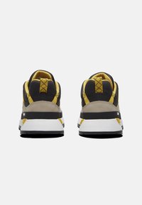 Zwarte en grijze sneakers met gele accenten. Heeft een gestructureerde bovenkant, een gepolsterde kraag en een witte, patronen zool voor grip en ondersteuning.