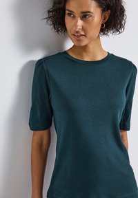 T-shirt teal à manches courtes avec un col rond. Fabriqué en tissu doux, avec de petites volants sur les épaules et une coupe décontractée.