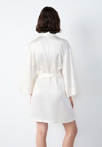 Morbido accappatoio in satin leggero di colore crema, con maniche larghe, una cintura e una texture liscia, con un taglio fino al ginocchio e dettagli minimi.