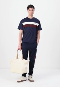 Marineblå T-shirt med hvide og maroon striber; marineblå sweatpants; cremefarvet tote bag; hvide sneakers med brune accenter; glat tekstur hele vejen igennem.