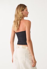 Top nero senza spalline con un design aderente e texture a costine, abbinato a pantaloni in denim bianco a vita alta con tasche posteriori.