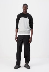 Felpa grigia e nera con maniche lunghe, colletto a girocollo e polsini a costine. Pantaloni cargo neri con tasche. Sneakers grigie con suole texturate.
