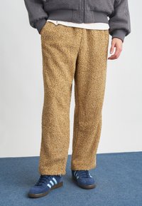Pantalones de pierna ancha en color beige con textura de forro polar y una superficie suave. Combinados con zapatillas de deporte en color azul marino con rayas en azul claro.
