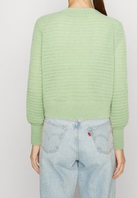 Ljusgrön, strukturerad stickad tröja med rund halsringning och långa ärmar, kort passform, kombinerad med ljusblå, högmidjade jeans.