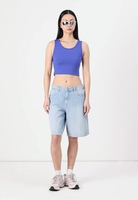 Crop top bleu, shorts en denim bleu clair, baskets blanches avec des accents gris, et lunettes de soleil réfléchissantes. Tenue simple et décontractée au design minimal.