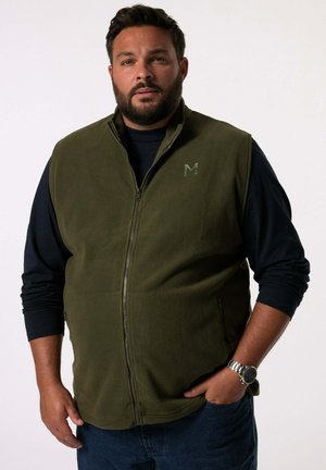 Chaleco de forro polar verde olivo con un cuello alto, cierre de cremallera en la parte delantera y un logotipo sutil en el pecho, usado sobre una camisa de manga larga oscura.